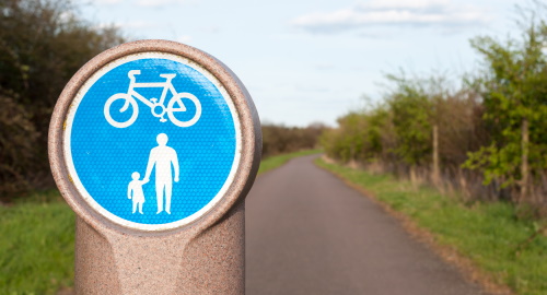 This image: This image is an illustrative photo of a cycling/pedestrian route surrounded 
					by greenery.
					The map: The map shows indicative residential development areas and a local centre in the 
					north-eastern part of the site, overlaid with indicative cycle and pedestrian routes, and locations
					of vehicle access to the site and to the development parcels. There are interactive markers which show 
					illustrative photos of cycling and walking routes when clicked on.